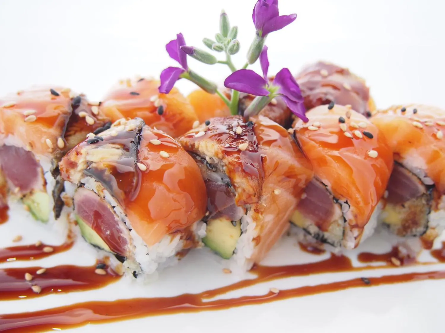 Salmon tuna sushi roll glazed with teriyaki sauce and garnished with purple flowers