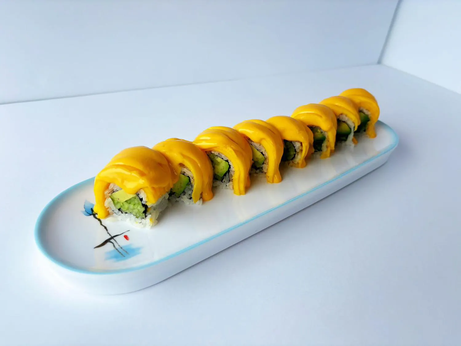 Mango sushi roll slices topped with bright mango sauce on decorative white plate