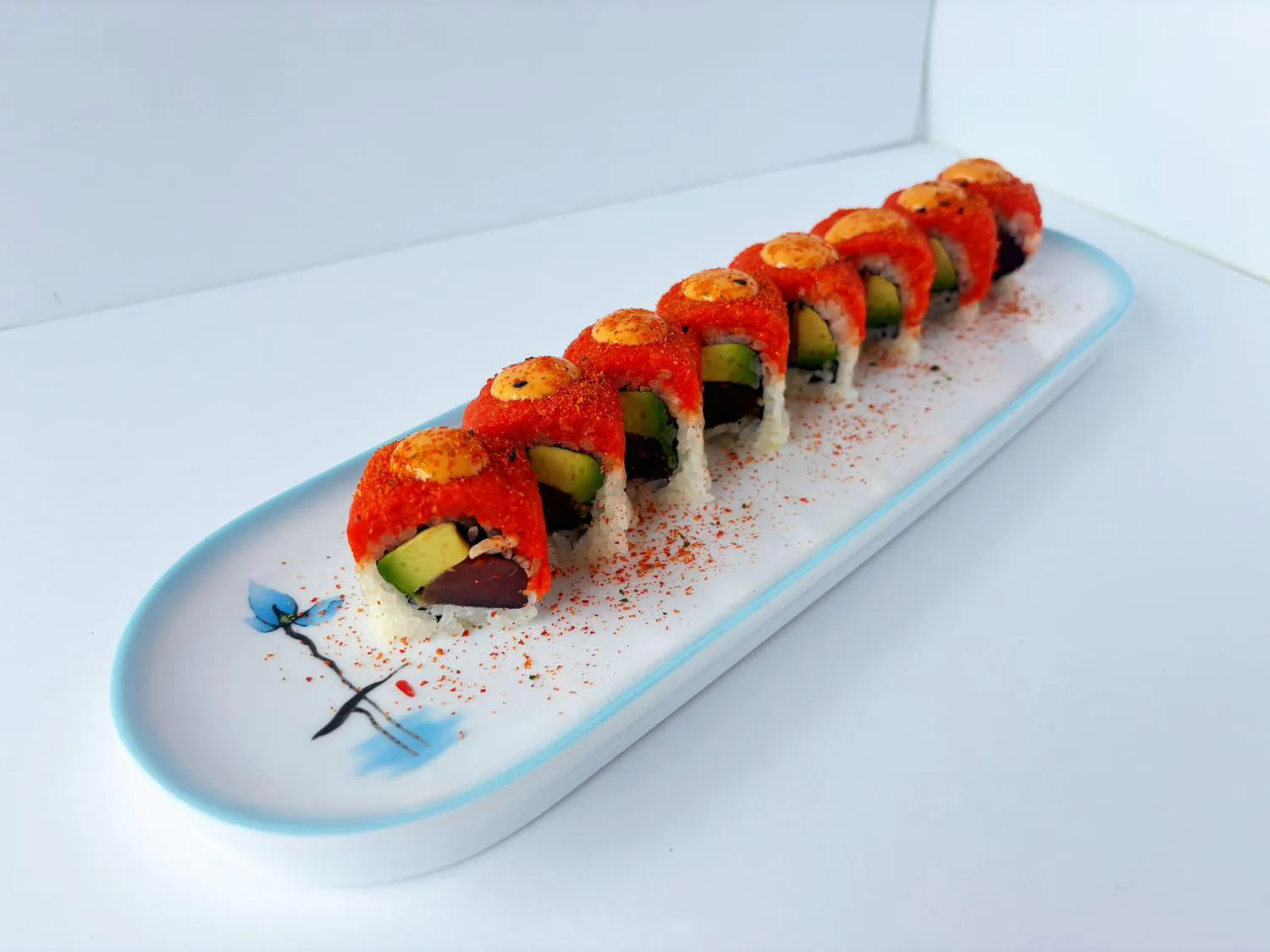 Sushi roll with red tobiko topping, avocado and tuna inside on long white plate