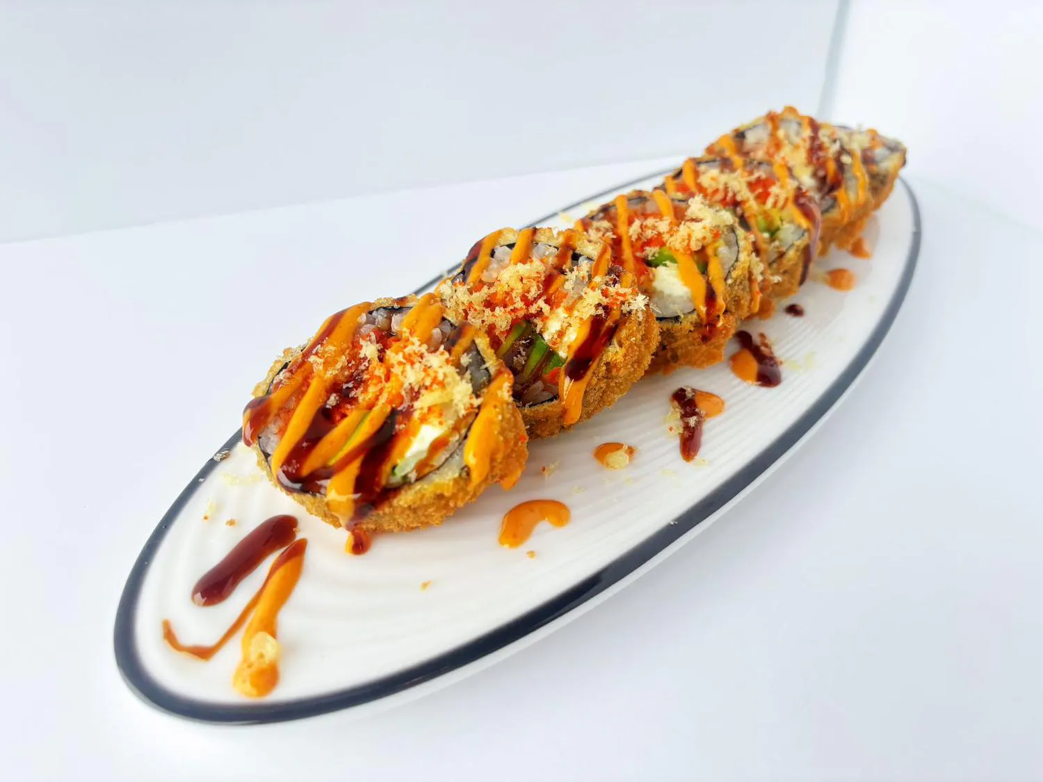 Deep fried crispy sushi roll drizzled with spicy and sweet sauces on oval plate