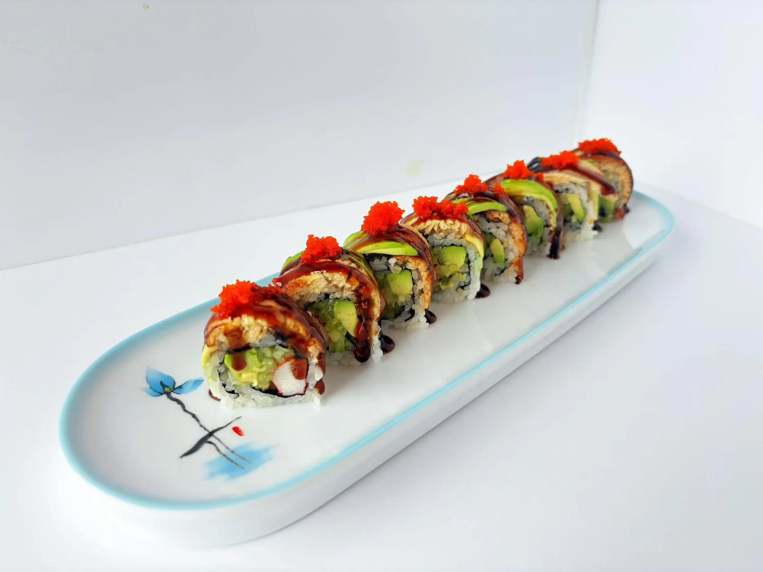 Sushi roll with eel, avocado and red tobiko garnish on long decorative plate